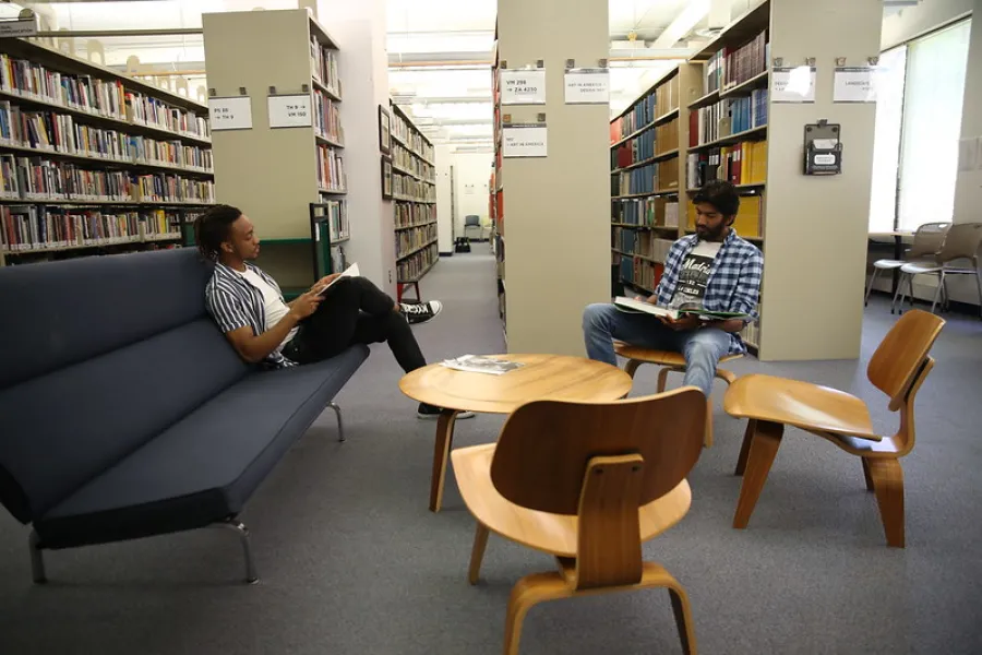 Two students reading on lounge seating between library stacks