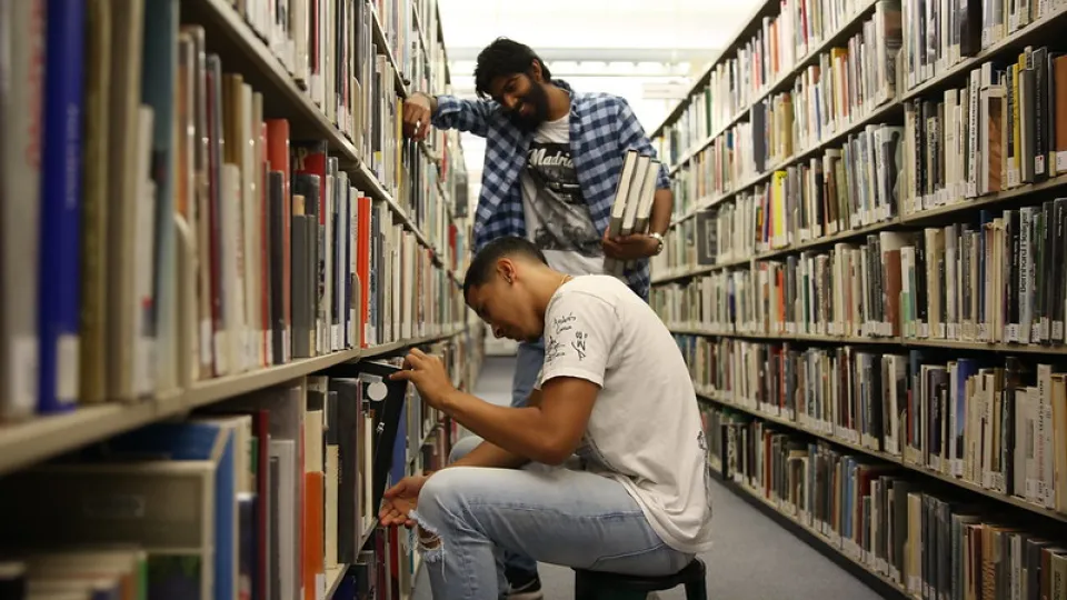 Two students browsing books in a narrow library stacks aisle