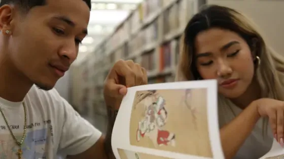 Two students looking closely at a printed illustration in the library stacks