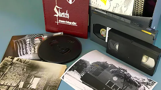 A yearbook, film reel, VHS tapes, and archival photographs on a blue table
