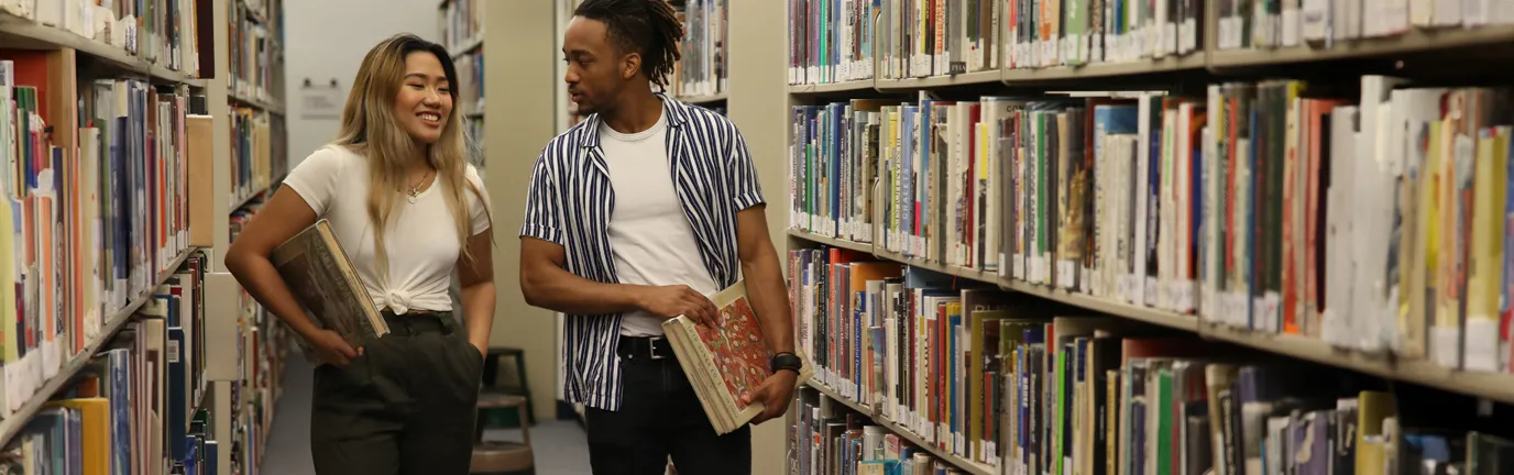 Two students walking through the OCAD U library stacks, carrying books